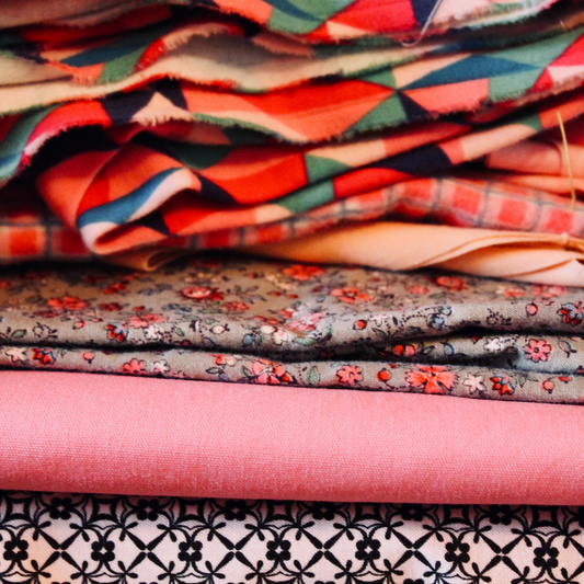 A pile of uncut fabric in shades of coral and pink. 
